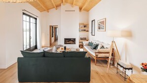 Una sala moderna con un sofá verde, suelo de madera, chimenea y un ventanal grande.