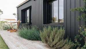 Un edificio moderno con fachada oscura, ventanas amplias y una terraza de madera con una hamaca.