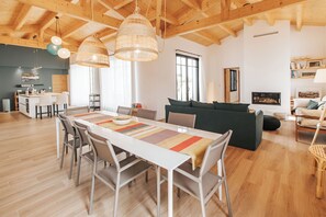 A spacious living area with a wooden ceiling, a dining table with chairs, a sofa, and a fireplace.
