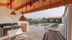 Un espacio al aire libre techado con piscina, terraza de madera y zona de barbacoa.