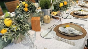 Una mesa dispuesta para una comida, decorada con limones, copas de cristal transparente y un mantel blanco.