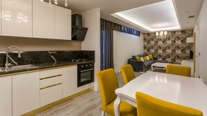 Una cocina moderna con encimera negra, armarios blancos y horno integrado. Hay un comedor con una mesa blanca y sillas amarillas.