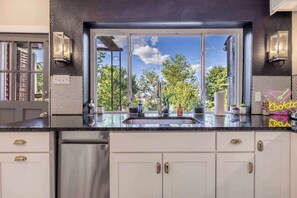 Een moderne keuken met een groot raam, witte kastjes, roestvrijstalen apparatuur en decoratieve voorwerpen op het aanrecht.