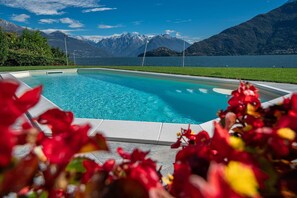 Ein Schwimmbecken mit klarem, blauem Wasser, umgeben von viel Grün und Bergen im Hintergrund.