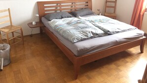 Un lit simple avec une tête de lit en bois, une table de chevet avec une lampe et une chaise.