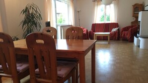 Un coin repas comprenant une table et des chaises en bois, un ensemble de canapés, une plante en pot et un réfrigérateur.