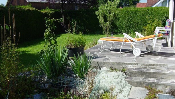Un jardin agrémenté d’une terrasse en pierre, de chaises longues et de diverses plantes.