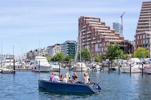 A boat with passengers, docked near a marina with various boats and buildings in the background. - 35th Floor Panorama Ocean View Apartment (Aarhus)
