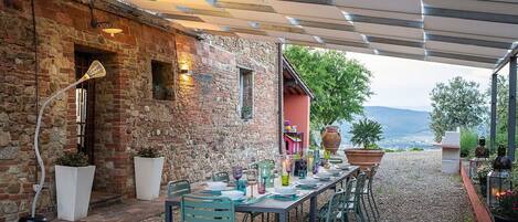 An outdoor dining area with a stone wall, a long table set for a meal, and a view of the landscape.