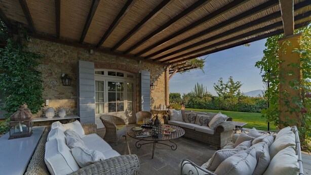 Une terrasse extérieure aménagée avec des meubles en osier, un mur en pierre et une vue sur la campagne.