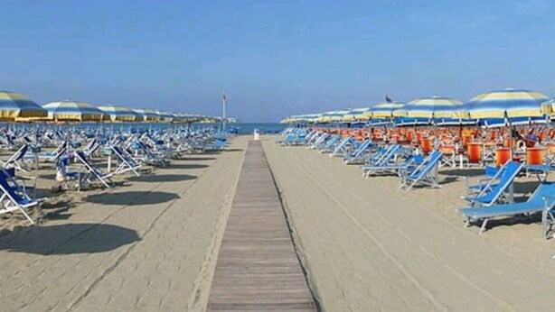 Une plage bordée de rangées de chaises longues et de parasols, une promenade en bois et un ciel dégagé.