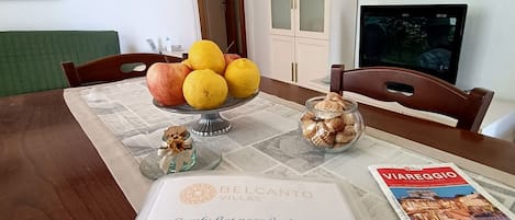 A dining table with a fruit bowl, a glass jar, a corkscrew, and a house book.