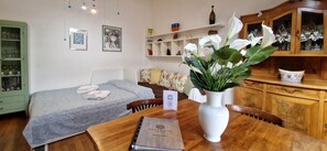Ein Hotelzimmer mit einem Bett, einem Holztisch mit einem Buch, einer Vase mit Blumen, einem Sessel, einem Schrank und Regalen mit Dekoration.