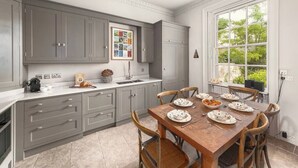 A modern kitchen with grey cabinets, a wooden dining table set for six, and a large window providing a view of greenery. - 3-bedroom Georgian maisonette (Bath and North East Somerset)
