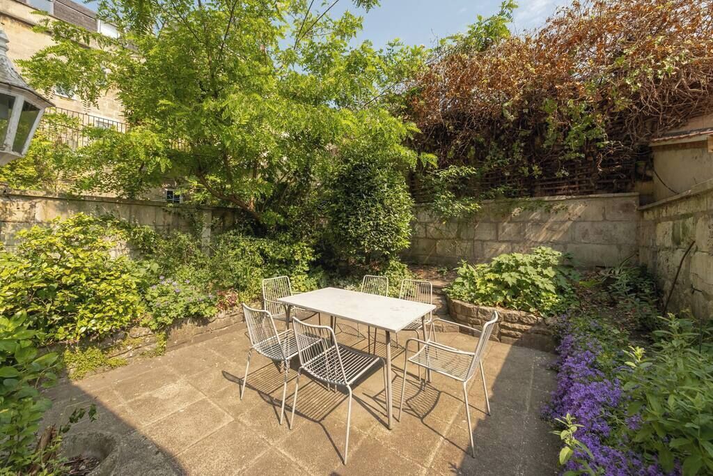 Un patio con tavolo e sedie, immerso nel verde e delimitato da un muro in pietra.