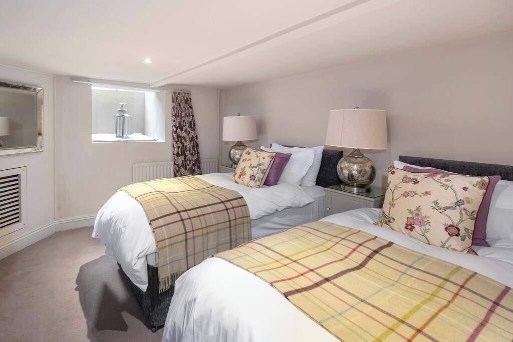 A hotel room with two beds, a window with curtains, a radiator, and two bedside lamps.