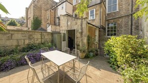 A stone building with a courtyard featuring a table and chairs, surrounded by plants and a stone wall. - 3-bedroom Georgian maisonette (Bath and North East Somerset)