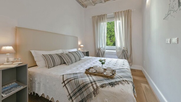 Een slaapkamer met een bed, nachtkastjes, een raam met gordijnen en uitzicht op groen.