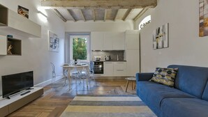 Een moderne woonkamer met een blauwe bank, een tv op een witte, lage kast, en een eethoek met transparante stoelen.