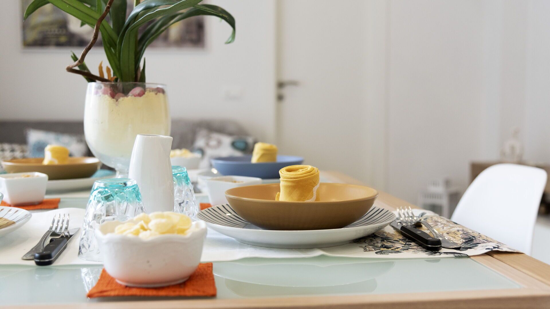 A dining table set with various dishes, including a bowl of yellow food, a white bowl with a yellow substance, and a glass with a blue pattern.