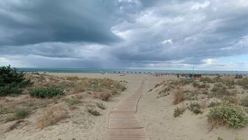 A sandy beach with a wooden boardwalk leading to the water, under a cloudy sky.