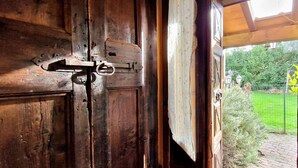 A wooden door with a metal latch, leading to an outdoor area with a green lawn and a brick pathway.