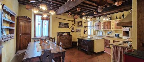 Uma cozinha rústica com armários de madeira, uma mesa de madeira e panelas de cobre penduradas.