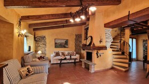 A rustic interior with a stone fireplace, wooden beams, a staircase, and a cozy seating area.