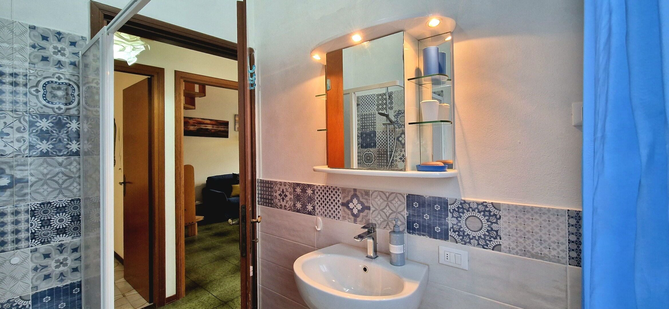 Une salle de bain avec des carreaux décorés, un lavabo, un miroir et une étagère contenant des articles de toilette.