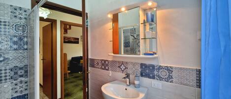 Une salle de bain avec des carreaux décorés, un lavabo, un miroir et une étagère contenant des articles de toilette.