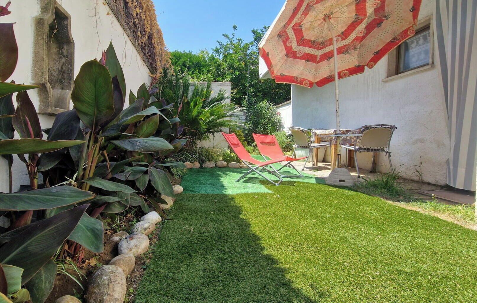 Ein gepflegter Garten mit Rasen, roten Stühlen und einem Zierteil-Sonnenschirm.