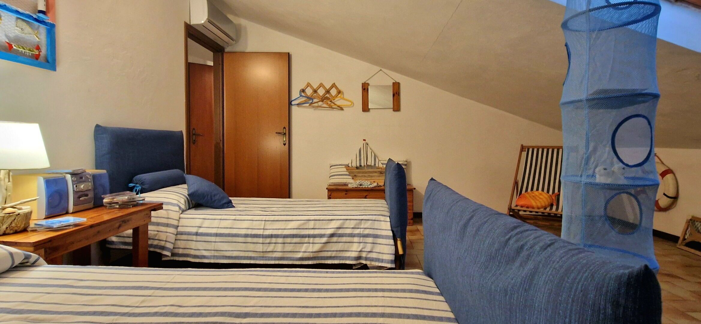 Una habitació amb dos llits, una taula de nit de fusta, una làmpada i una taula petita amb una ràdio i llibres.