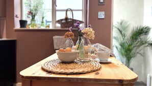 Una mesa de madera con un posavasos tejido, un cuenco de huevos y dos botellas de vidrio con flores.