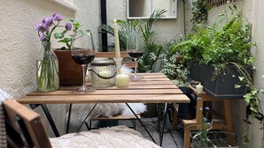 Una mesa de madera con un jarrón de flores moradas, dos copas de vino y velas en un jardín.