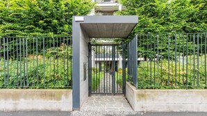 A gated entrance with a stone pathway leading to a building, surrounded by greenery and metal fences. - City Oasis · Terrace and swimming pool (Milano)