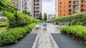 A rooftop pool area with stone flooring, surrounded by lush greenery and modern apartment buildings. - City Oasis · Terrace and swimming pool (Milano)