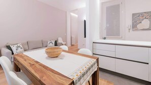 Un espace repas moderne avec une table en bois, des chaises blanches et une cuisine en arrière-plan.