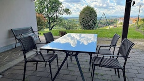 Une terrasse extérieure avec une table et des chaises, entourée d’un sol en pierre et offrant une vue sur la campagne.