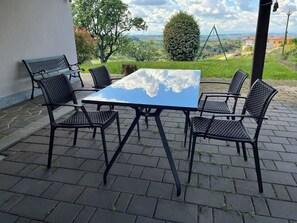 An outdoor patio with a table and chairs, surrounded by a stone floor and a view of the countryside.