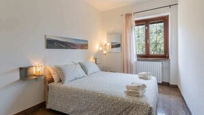 A bedroom with a bed, bedside lamps, a window with curtains, a radiator, and a painting on the wall. - Panorama villa nestled among the vineyards, Langhe (Bricco di Neive)