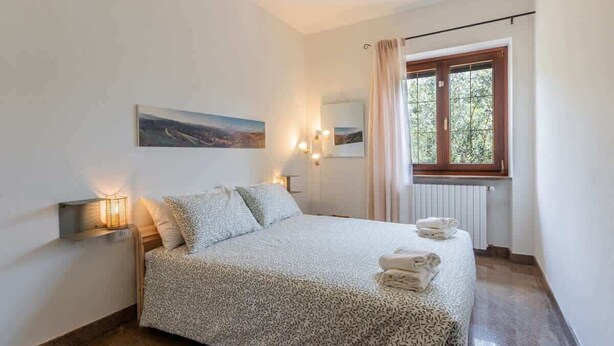 Une chambre à coucher avec un lit, des lampes de chevet, une fenêtre avec des rideaux, un radiateur et un tableau au mur.