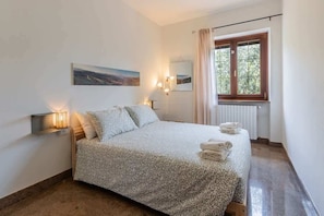 Ein Schlafzimmer mit Bett, Nachttischlampen, einem Fenster mit Vorhängen, einer Heizung und einem Bild an der Wand.