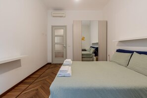 Ein Schlafzimmer mit einem Bett, einer Tür, einem Spiegel und einem kleinen Tisch mit einer Lampe.
