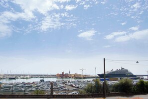 A marina with parked cars, a large cruise ship docked, and a building with a tower in the background.