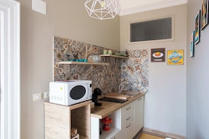 A compact kitchen with a microwave, wooden cabinets, a sink, and decorative tiles.