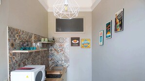 A compact kitchen with a microwave, shelves, and a hanging light fixture. - Charming Studio Verga, by the old town (Catania)