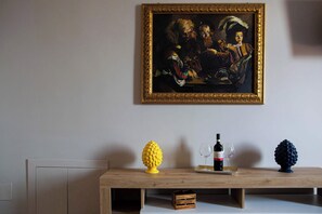 Ein Gemälde an der Wand, ein Holztisch mit Flasche und Gläsern sowie zwei Dekorationsobjekte.