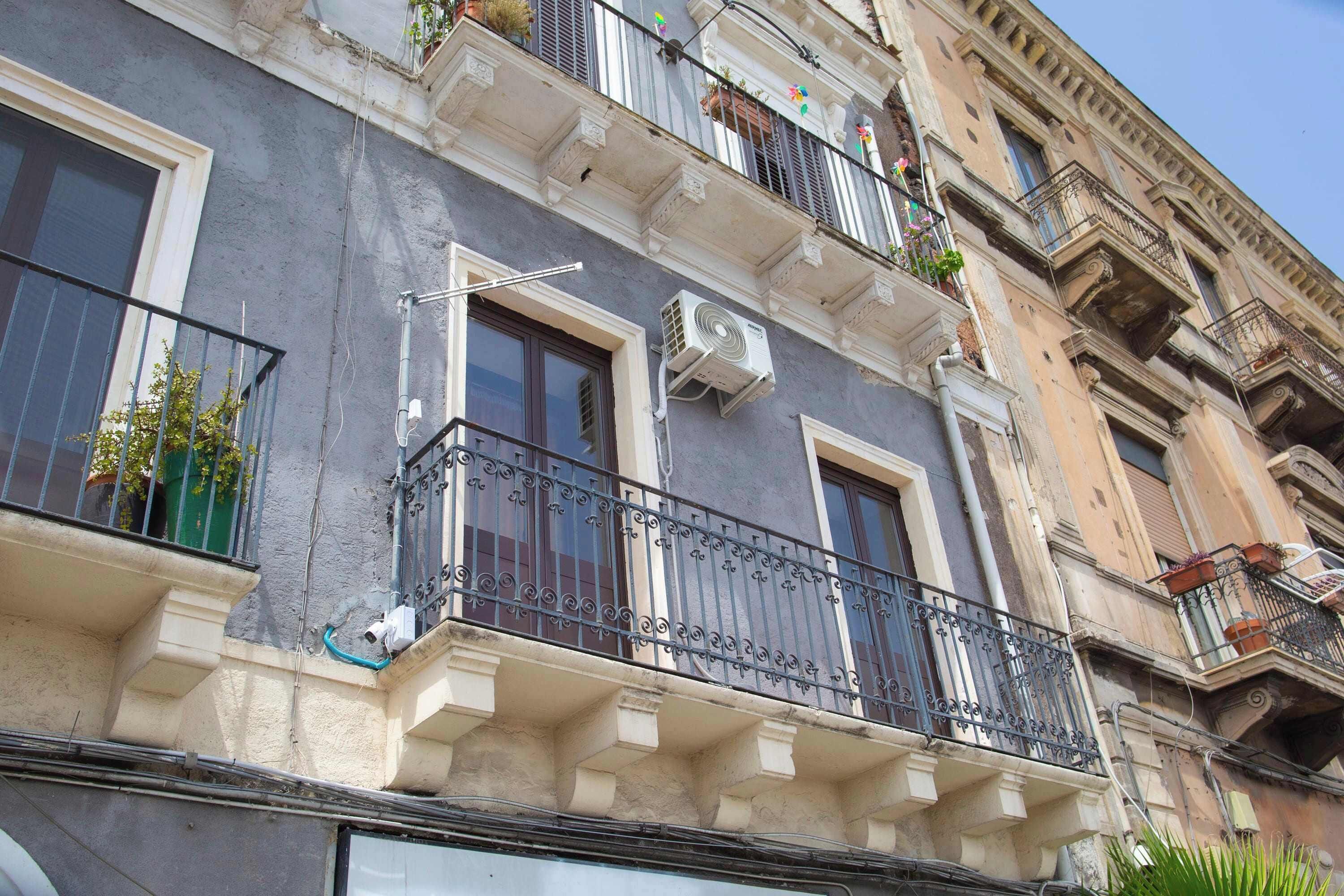 Un immeuble à plusieurs étages doté de balcons, de climatiseurs et d’une fenêtre avec un rideau.