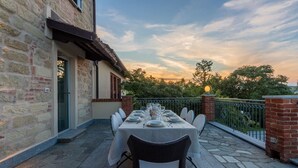 An outdoor dining area with a table set for six, surrounded by stone walls and a metal railing. - Ca' Vecchia, private padel & pool (Province of Alessandria)