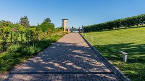 A paved pathway leading to a tower-like structure in a landscaped area with grass and trees. - Ca' Vecchia, private padel & pool (Province of Alessandria)